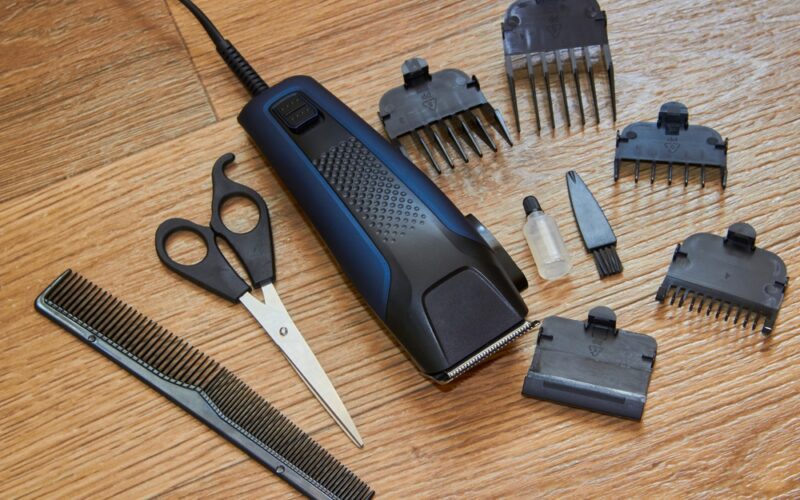 Elektrický strojek na vlasy s nástavci, nůžkami, hřebenem a olejíčkem na dřevěném pozadí