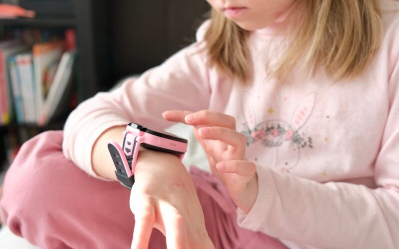 Holčička v růžových šatech má na ruce růžovo-černé smart hodinky
