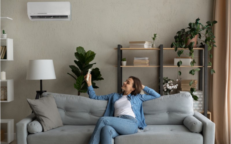 Topení klimatizací - žena na gauči zapíná klimatizaci