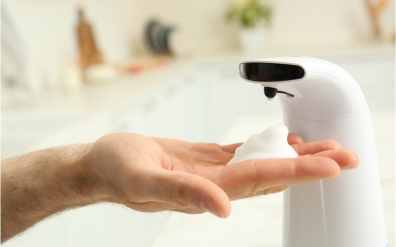 Muž si dávkuje mýdlo pomocí bílého bezdotykového dávkovače
