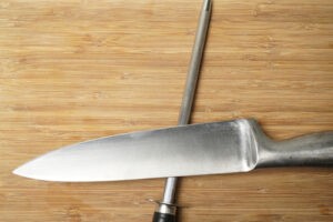 Nerezová kulatá bruska na nože a nůž na dřevěném pozadí